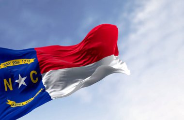 Kuzey Carolina bayrağının fotorealistik 3D görüntüsü dinamik bir şekilde açık bir gökyüzü altında dalgalanıyor. Vatansever bir özgürlük ve gurur sembolü. Kültürel ve tarihi temalar için ideal..