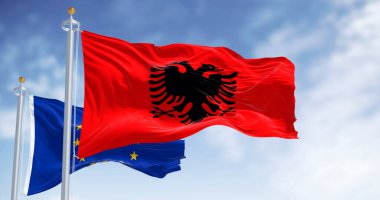 Siyah çift başlı kartal ve rüzgarda dalgalanan Avrupa Birliği bayrağıyla kırmızı Arnavut bayrağı birlik, diplomasi ve Avrupa kimliğini simgeliyor.
