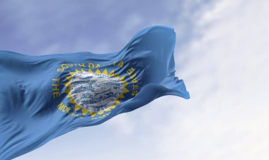 Güney Dakota bayrağının rüzgarda dalgalanan eyalet mührü ile yakın çekimi, gurur, özgürlük ve kimliği simgeleyen güneş ışınlarını içeriyor. Dokuma dokusunun gerçekçi 3B görüntüsü