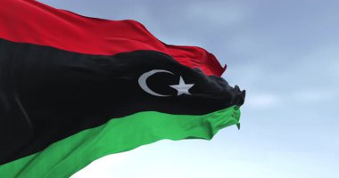 Açık bir günde Libya bayrağı sallanıyor. Kırmızı, siyah, yeşil çizgiler; beyaz yıldız ve siyah üzerine hilal. Kusursuz 3 boyutlu animasyon. Yavaş çekim döngüsü. Seçici odak