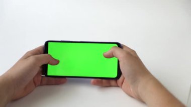 Yeşil ekranlı, ışık arkaplanlı bir telefonun elinde.