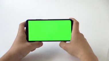 Yeşil ekranlı, ışık arkaplanlı bir telefonun elinde.
