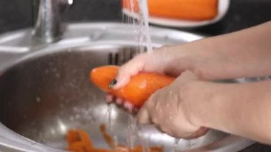 Kadın elleri akan suyun altında havuç yıkar.