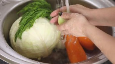 Kadın elleri sebzelerin arka planında akan suyun altında soğan yıkıyor.