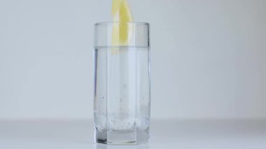 Limon dilimleri şeffaf bir bardak suya düşer.