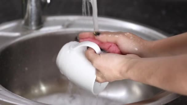 女用手在流动的水中用泡沫冲洗一个白色的杯子 — 图库视频影像