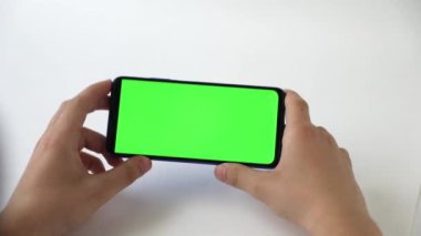 Yeşil ekranlı, ışık arkaplanlı bir telefonun elinde.