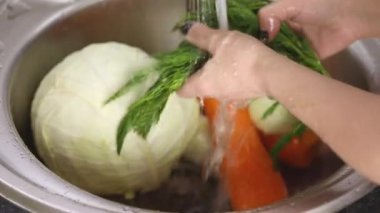 Kadın elleri akan suyun altında dereotu yıkar.