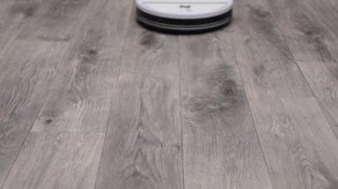 Beyaz robot elektrik süpürgesi gri zemini temizliyor.
