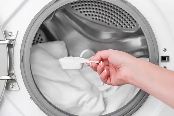 Çamaşır makinesinin arka planında çamaşır tozuyla kaşık tutan kadın..