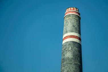 Mavi gökyüzünün altındaki tuğla ocağının sütunları. Çamurdan yapılmış çiğ tuğlalar ateşlenir ve bu sütunlardan duman çıkar.