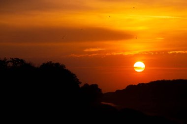 Çarpıcı bir günbatımı, turuncu, pembe ve morun canlı tonlarıyla gökyüzünü boyar. Altın ışık manzaranın üzerine yansıyarak huzur verici ve büyüleyici bir manzara yaratıyor. Mükemmel bir an, günün sonunda güzelliği yakalıyor.