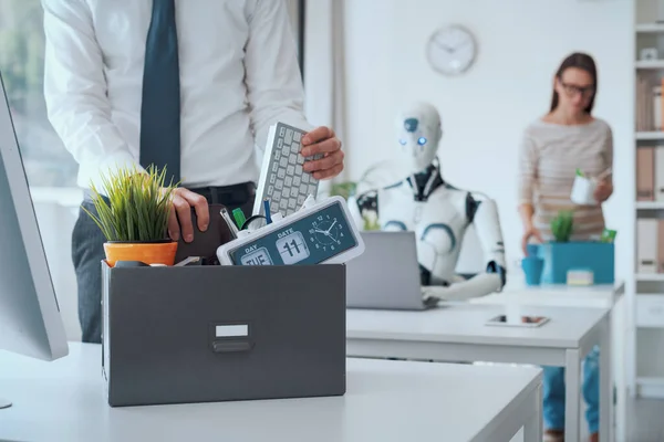 解雇されたビジネス関係者が荷物をまとめてオフィスを出ると ロボットが机に座って作業しています Aiが仕事に与える影響 — ストック写真