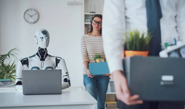 解雇されたビジネス関係者が荷物をまとめてオフィスを出ると ロボットが机に座って作業しています Aiが仕事に与える影響 — ストック写真