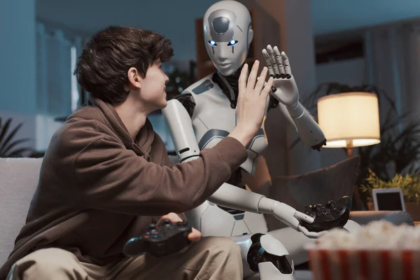 Happy boy and AI robot giving a high five, they are playing videogames together at home, human-robot interaction concept