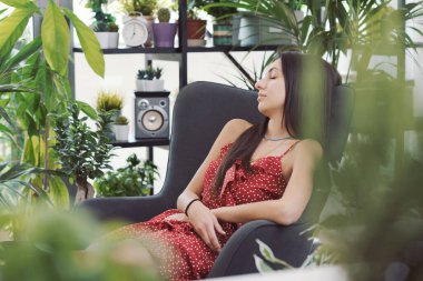 Evinde güzel bitkilerle çevrili genç ve çekici bir kadın, bir koltukta uyuyor.