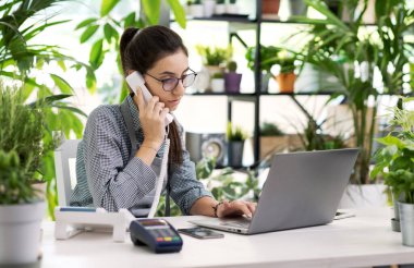 Profesyonel çiçekçi masasında oturuyor ve çalışıyor, telefonla emirler alıyor.