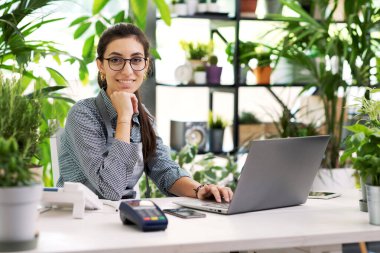 Profesyonel bir çiçekçi masada oturuyor ve laptopuyla çalışıyor.