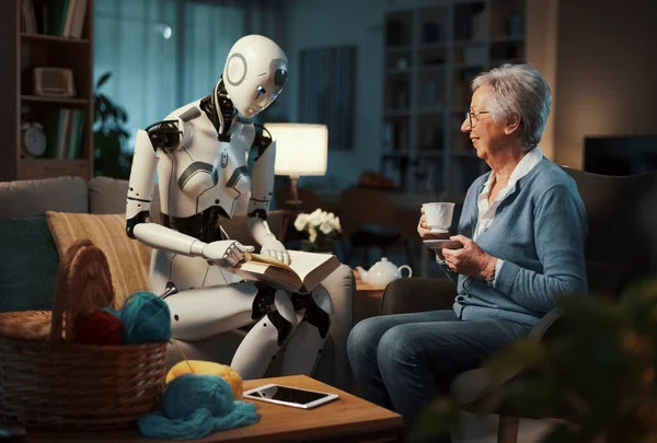 一位老年妇女享受着下午茶 让她的机器人助手给她读一本小说 未来护理和老年人护理的概念 — 图库照片
