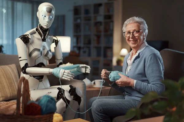 一位老年妇女在伴侣机器人的帮助下 在客厅的扶手椅上编织了一个纱球 — 图库照片
