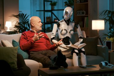 Kıdemli erkek ve dişi android robot evdeki kanepede oturuyor, birlikte kitap okuyorlar, insan-robot ilişkileri kavramı.