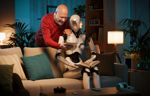 一个快乐的老人把他的平板电脑展示给一个女性人形机器人 他们正在一起呆在家里 — 图库照片