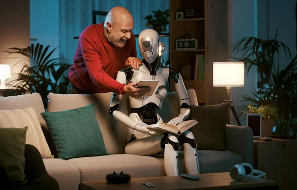 一个快乐的老人把他的平板电脑展示给一个女性人形机器人 他们正在一起呆在家里 — 图库照片
