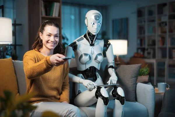 一个漂亮的小女孩和她配备了人工智能的家用机器人 一起选择看电视的内容 — 图库照片