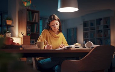 Genç üniversite öğrencisi gece geç saatlerde kitap okuyor ve sınavlarına hazırlanıyor.