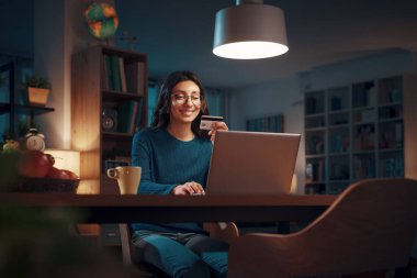 Happy woman holding a credit card and doing online shopping with her laptop clipart