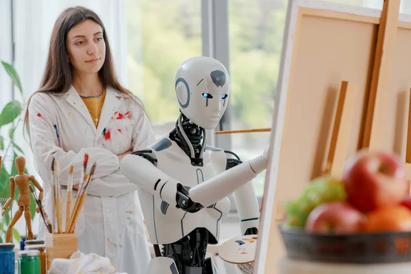 Creative AI robot learning how to paint on canvas in the art studio, a young teacher is training her