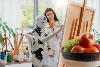Sanat stüdyosunda resim yapmayı öğrenen yaratıcı yapay zeka robotu genç bir öğretmen onu eğitiyor.