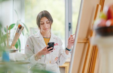 Sanat stüdyosunda çalışan genç bir sanatçı, akıllı telefonuyla internete bağlanıyor ve sohbet ediyor.