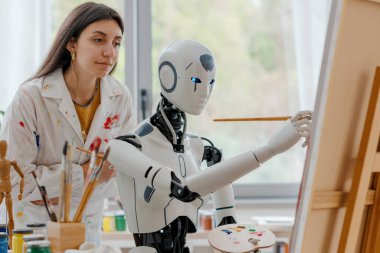 Sanat stüdyosunda resim yapmayı öğrenen yaratıcı yapay zeka robotu genç bir öğretmen onu eğitiyor.