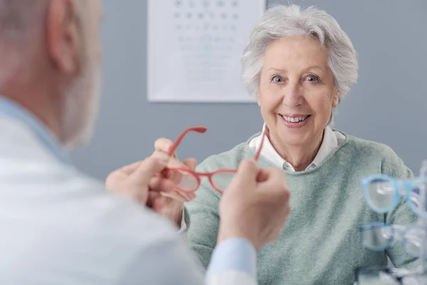 新しい処方箋メガネを試している笑顔の高齢女性 オキュリストは彼女を助けています — ストック写真