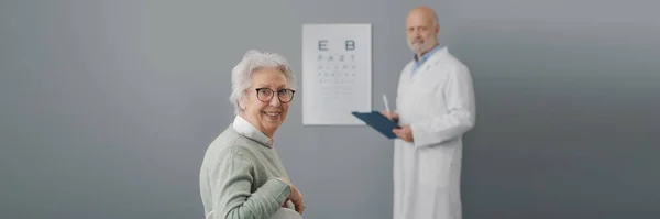 医者と眼科検査を受けるシニア女性 彼らはカメラで微笑んでいる — ストック写真