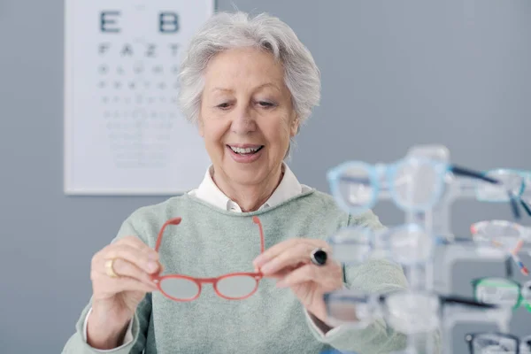 アイウェアショップでメガネを選択するシニア女性 彼女は眼鏡を保持し — ストック写真