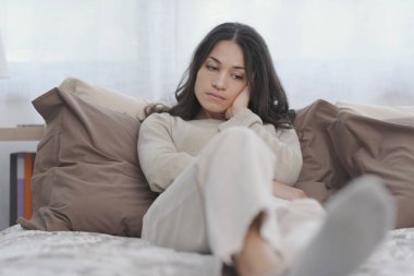 Sad young woman sitting on the bed at home, she is lonely and depressed