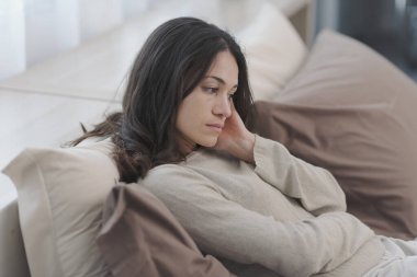 Sad young woman sitting on the bed at home, she is lonely and depressed