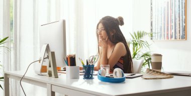 Genç yaratıcı kadın masada oturuyor ve bilgisayarıyla çalışıyor.