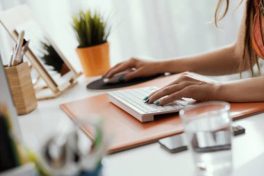 Masada oturan ve klavyeye yazan bir kadın, evden çalışıyor.