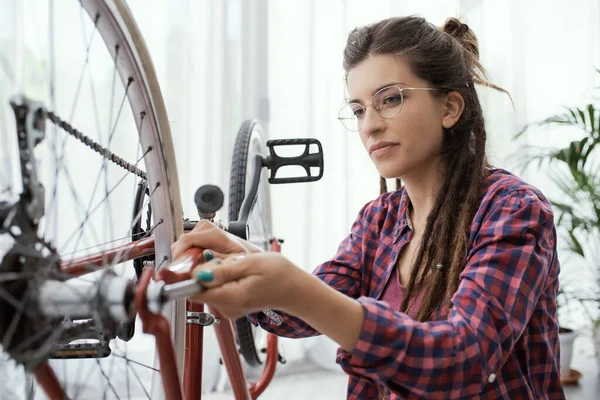 Evde kendi bisikletini tamir eden kendine güvenen bir kadın, bir anahtar kullanıyor ve tekerlekleri kontrol ediyor.