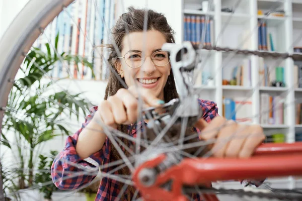 Evde kendi bisikletini tamir eden kendine güvenen bir kadın, bir anahtar kullanıyor ve tekerlekleri kontrol ediyor.