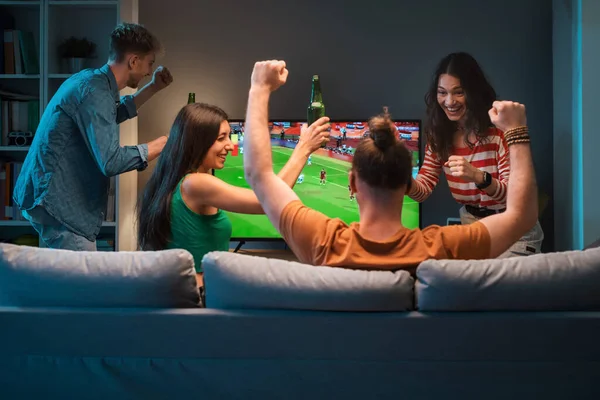 一緒にテレビでサッカーの試合を見ている若い友人のグループと彼らのチームのために応援 — ストック写真