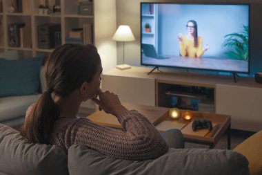 Kanepede dinlenen ve televizyonunda video izleyen bir kadın.