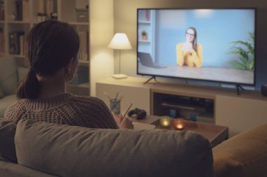 Kanepede dinlenen ve televizyonunda video izleyen bir kadın.