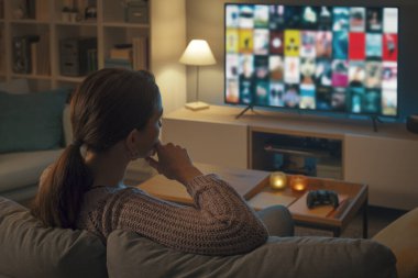 Kanepede dinlenen ve televizyonundan bir film seçen bir kadın.