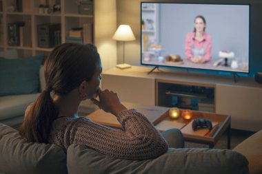 Kanepede oturan ve TV 'de yemek programı izleyen bir kadın, bir pasta şefi tatlı hazırlamayı öğretiyor.