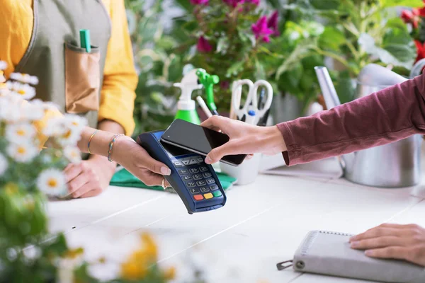 Müşteriler onun akıllı telefonunu, elektronik ödeme konseptini kullanarak çiçekçide ödeme yapıyor.