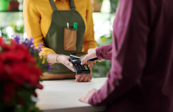 Customer paying in a flower shop using her smartphone, electronic payments concept